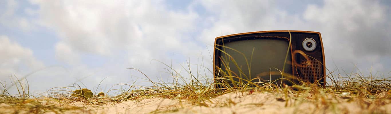 ein altmodischern Fernsehen liegt auf einer Düne vor blau-weißem Himmel