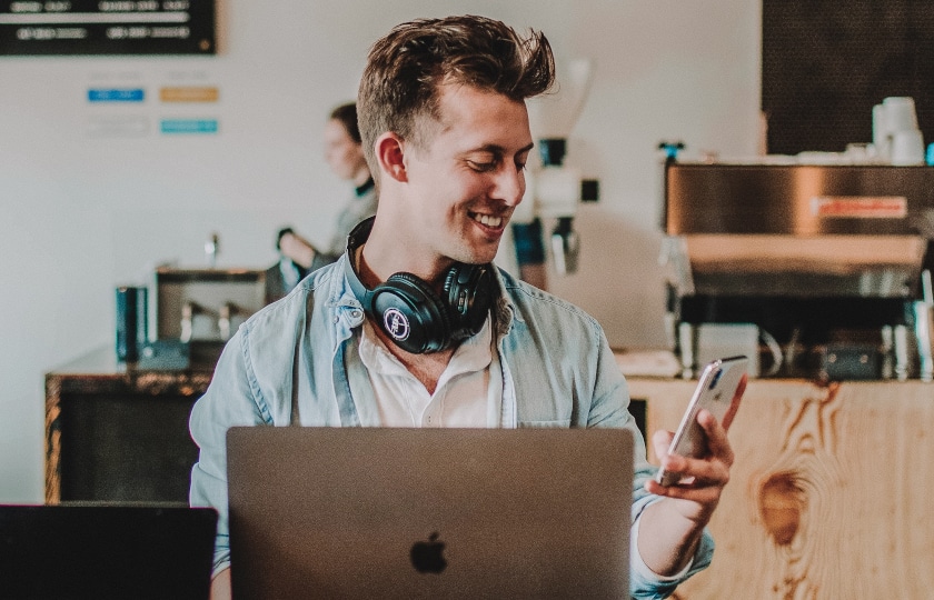 Junger Mann im Café mit Laptop und Smartphone