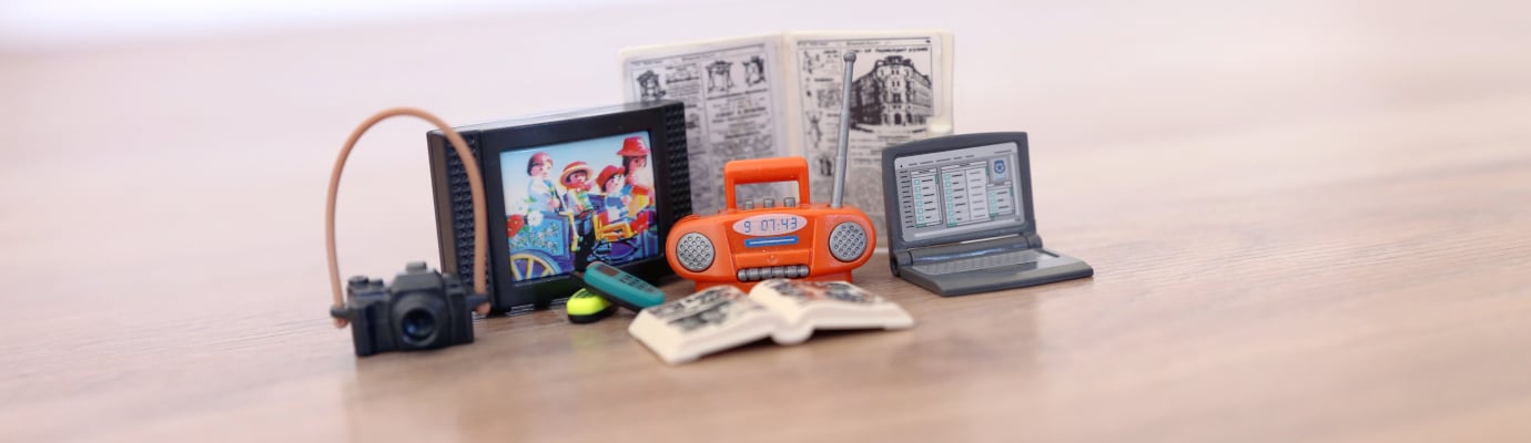 Spielfiguren und Playmobil-Gegenstände auf einem Haufen: Radio, Laptop, Fernseher, Kamera, Buch und Zeitung.