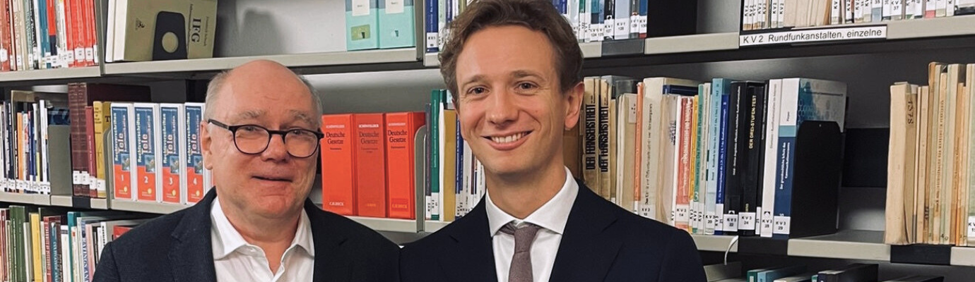 Wolfgang Schulz and Christian Ollig in front of a bookshelf.