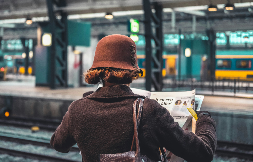 Eine Frau liest eine Zeitung an einem Bahngleis.