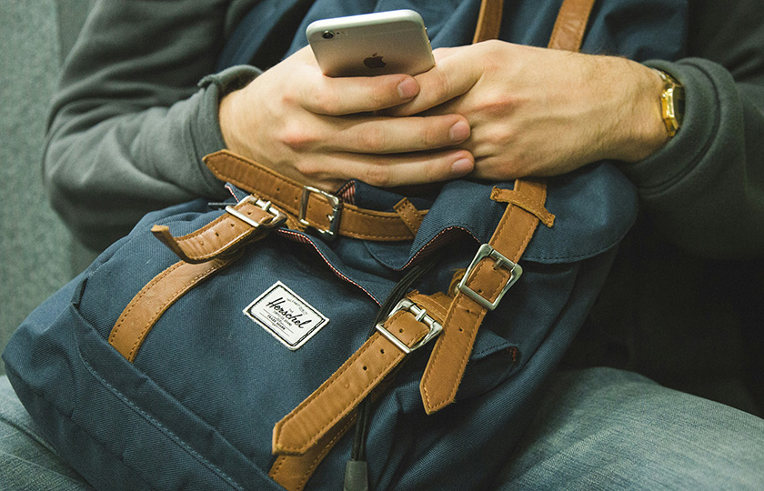 Junger Mann hält ein Handy in seinem Schoß